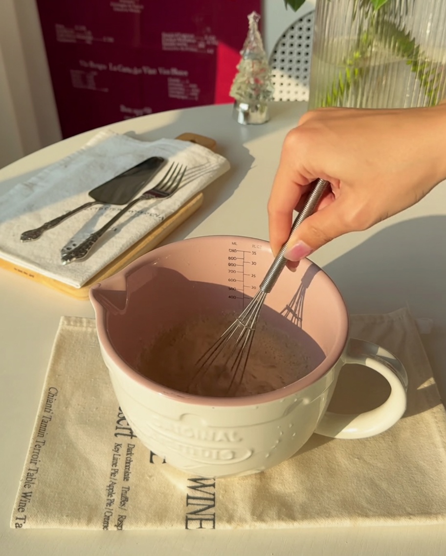 Close-up of a hand whisking yeast into warm water inside a pink measuring cup.