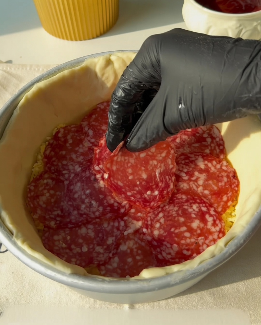 Bacon strips being placed on top of the salami layer.