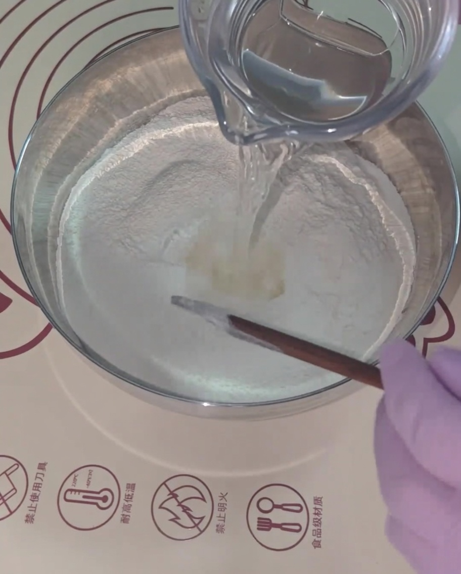 Warm water being poured into the flour mixture, being stirred with wooden chopsticks.