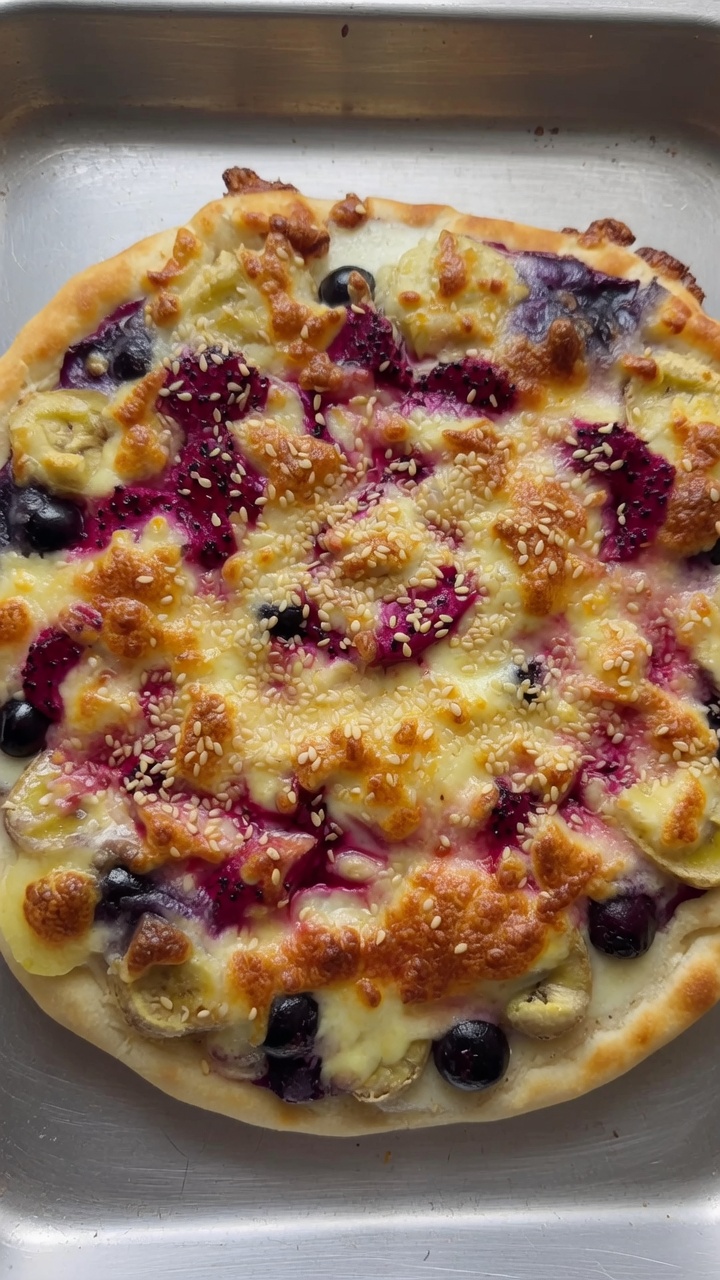 A freshly baked round fruit pizza featuring golden-brown crust, melted mozzarella cheese, and colorful fresh fruit toppings.