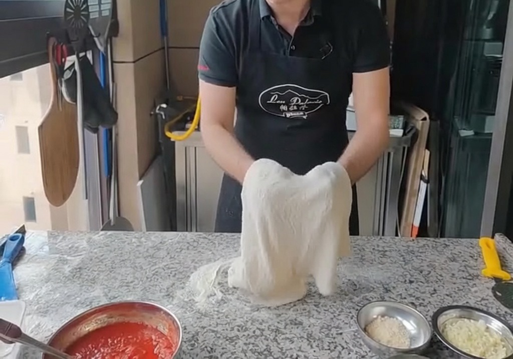 Stretching the pizza dough over the knuckles of both hands, holding it up vertically.