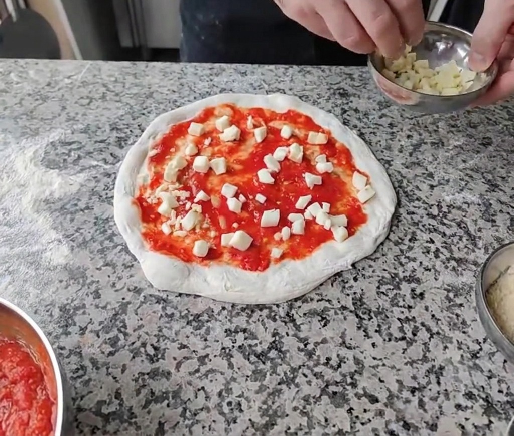 Sprinkling diced white cheeses evenly over the tomato sauce base on the pizza dough.