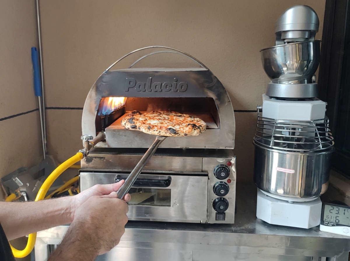 A perfectly baked pizza with a charred crust being removed from the oven on a metal peel.