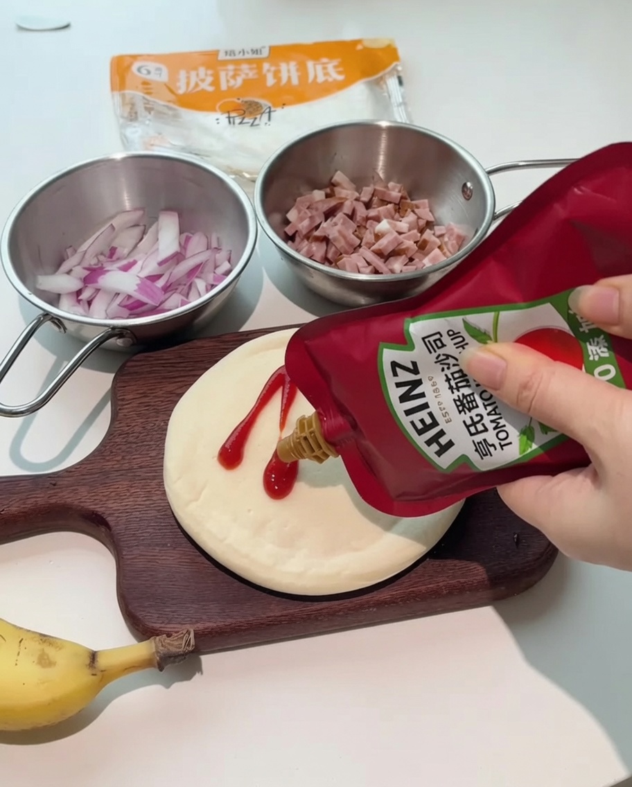 Bottles of ketchup and salad dressing being squeezed onto a round pizza crust on a wooden board.
