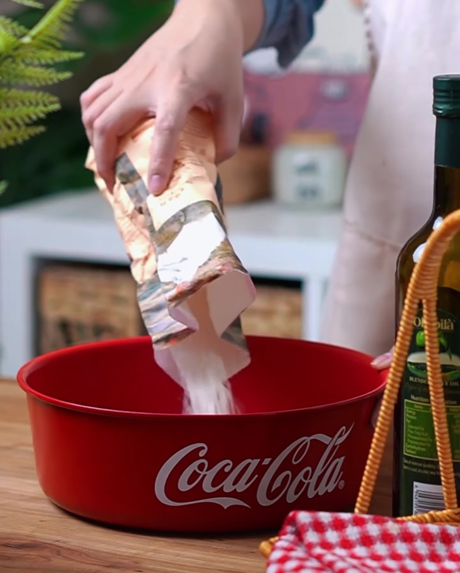 A close-up of high-gluten flour, yeast, and salt being poured into a red Coca-Cola bowl.