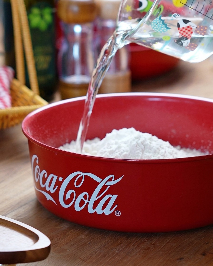Cold water being poured into the red bowl containing the flour mixture.