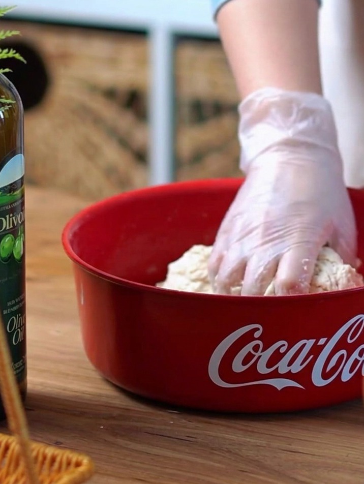Hand in a clear glove kneading dough inside a red mixing bowl.