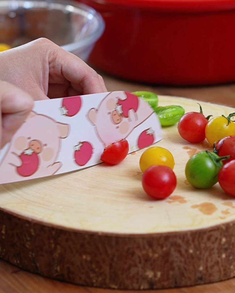 Cherry tomatoes being sliced in half on a wooden cutting board with a patterned knife.