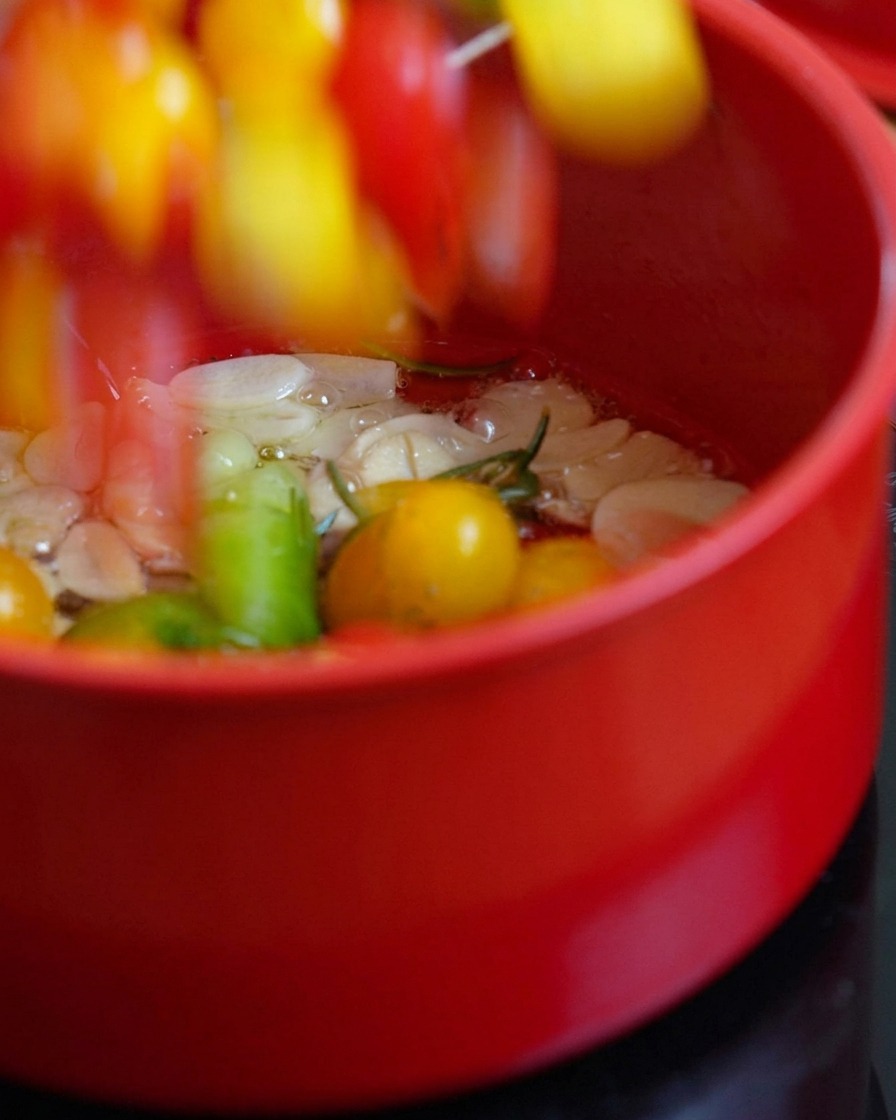 Halved cherry tomatoes being added into a pot of hot oil and herbs.
