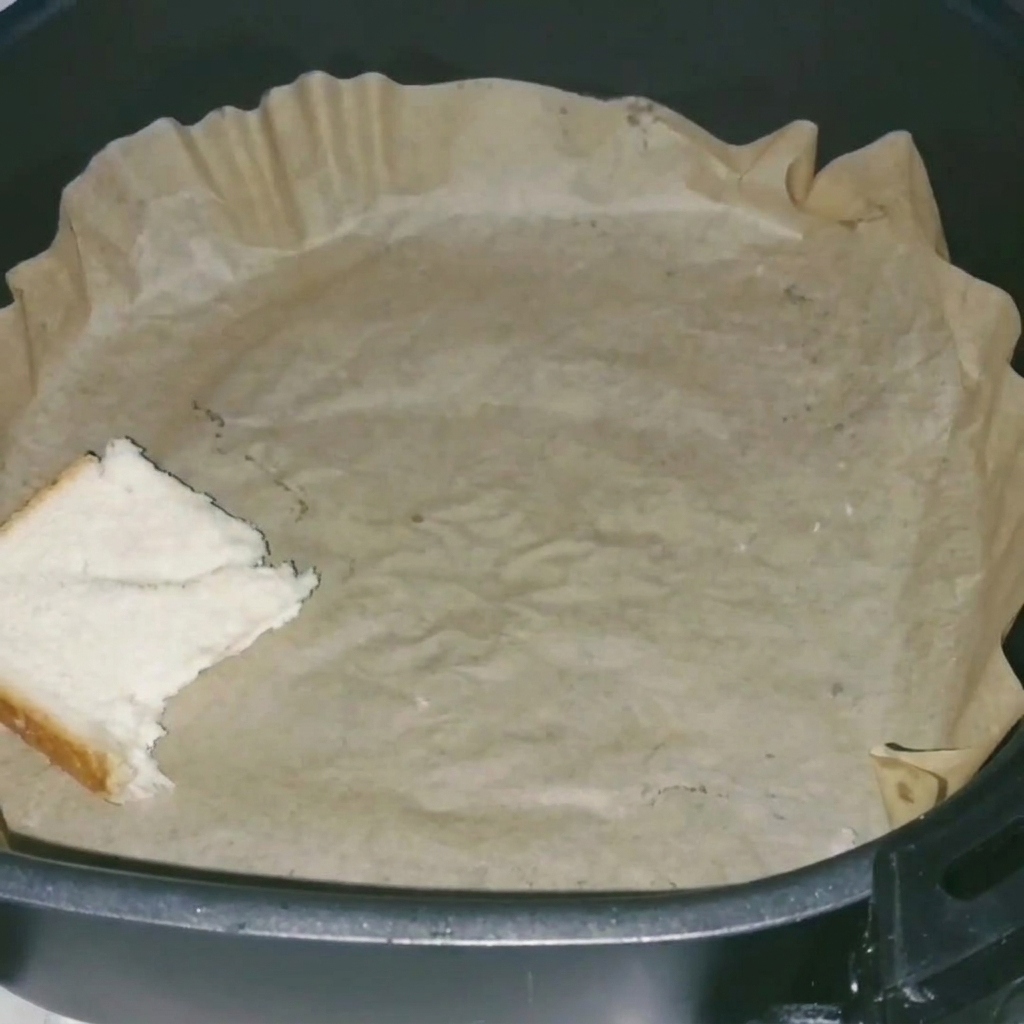 A close-up of white bread pieces neatly arranged in an air fryer basket lined with parchment paper.