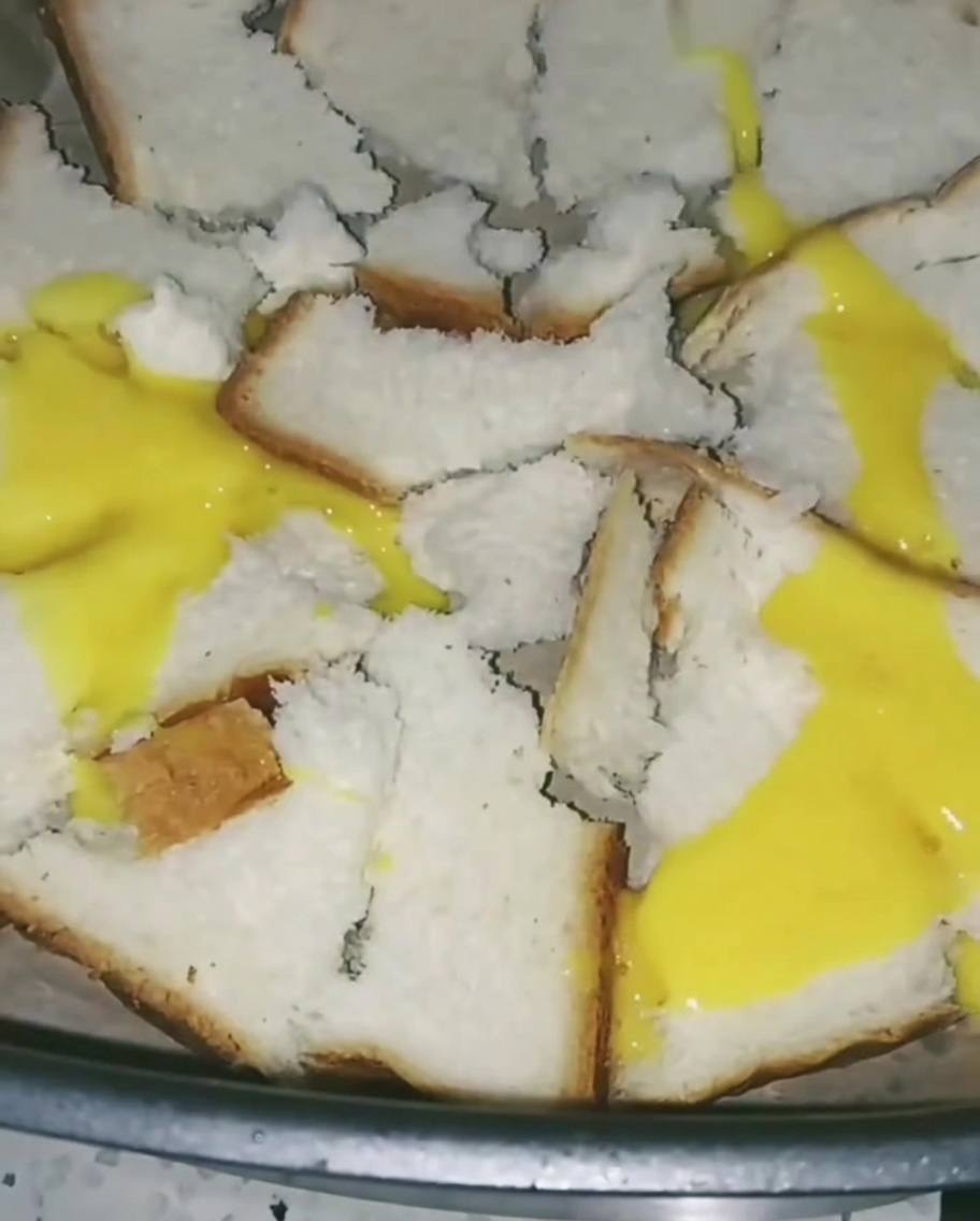 Beaten eggs being poured over bread in the air fryer, creating a thin, yellow layer across the pieces.