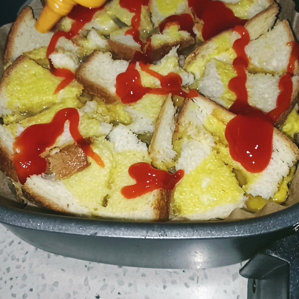 A brush spreading red tomato sauce over the cooked toast-and-egg base in the air fryer.
