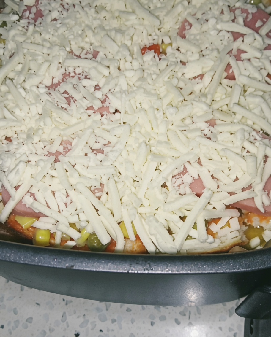 A close-up of a generous layer of shredded cheese covering the ham and vegetables in the air fryer basket.