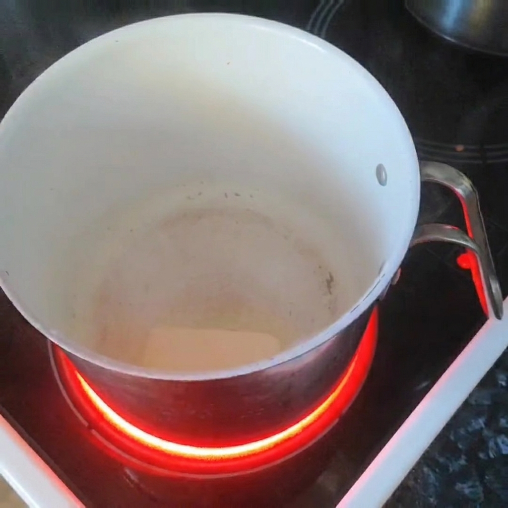 A knob of butter melting in a white saucepan on an induction stovetop.