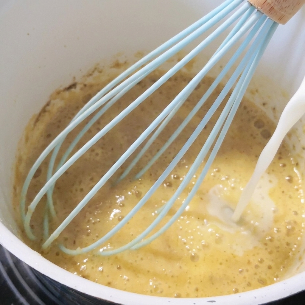 Milk being poured into the roux while whisking.