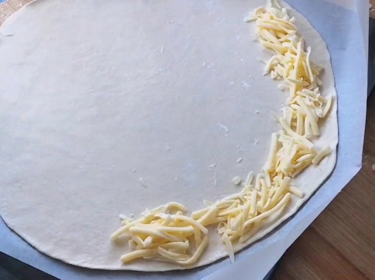 White sauce being spread onto a round pizza dough base.