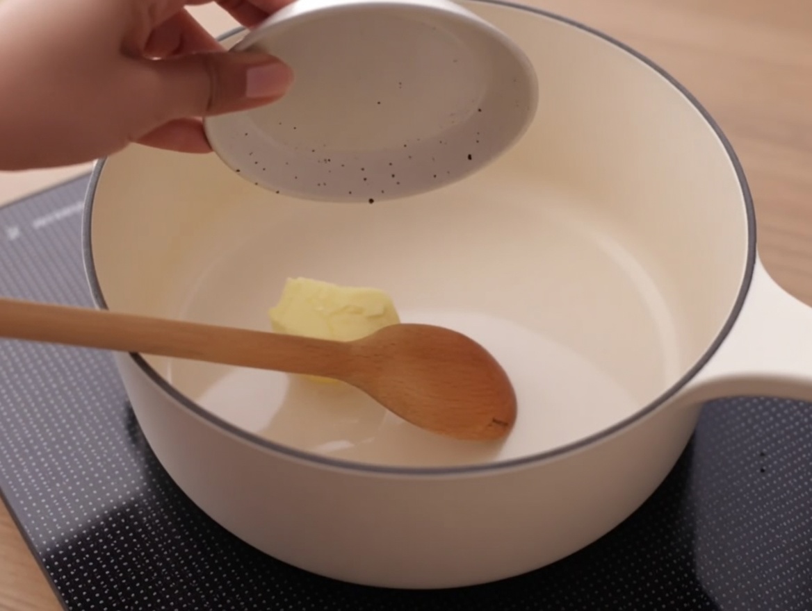 A knob of butter melting in a clean white saucepan on a stovetop.