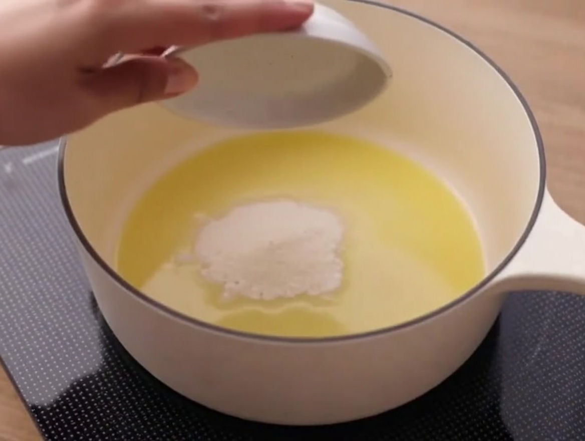 Flour being stirred into melted butter in a saucepan, forming a paste.