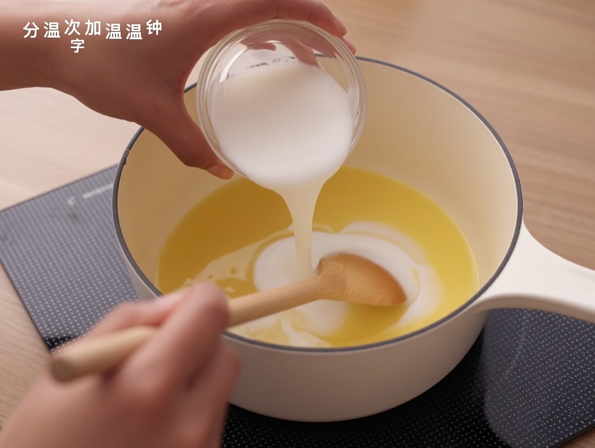 Milk being poured into a roux base in a saucepan, with a wooden spoon mixing it.
