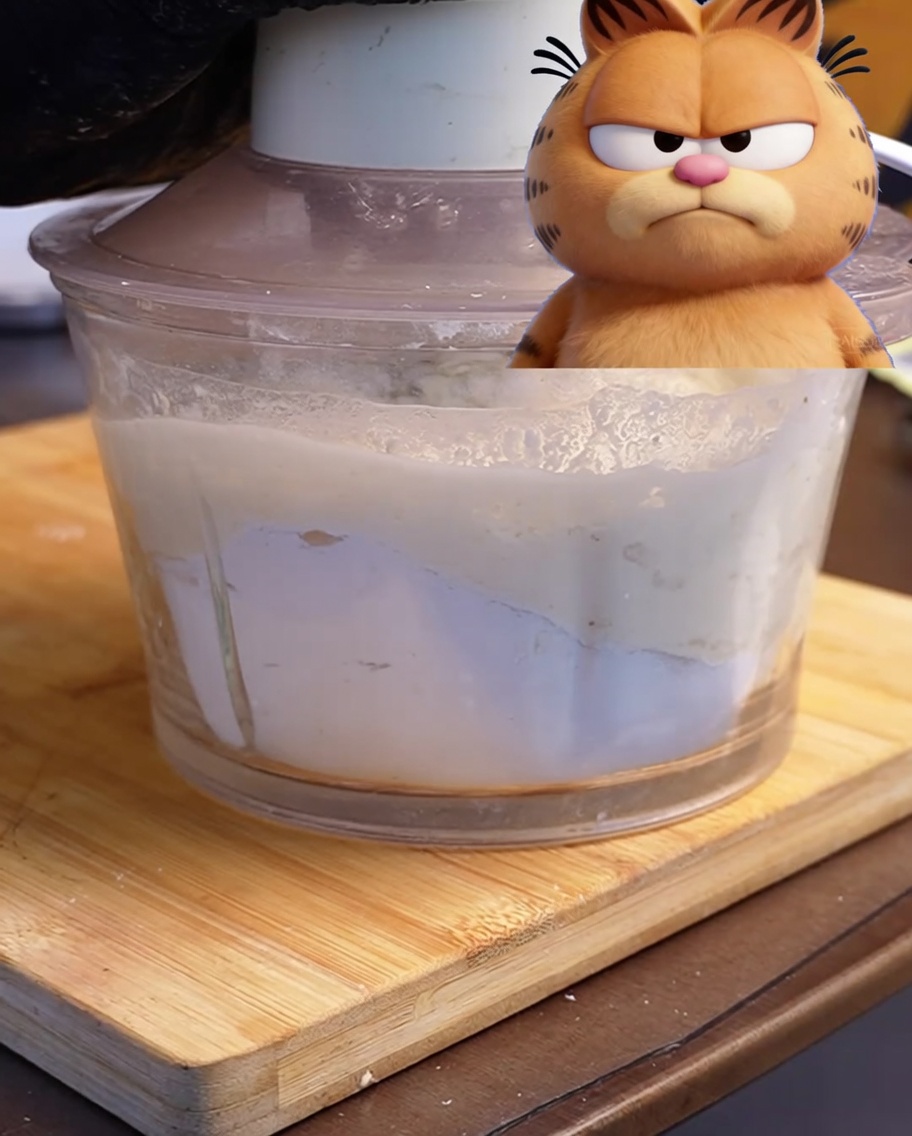 A food processor containing freshly mixed pizza dough ingredients on a wooden board.