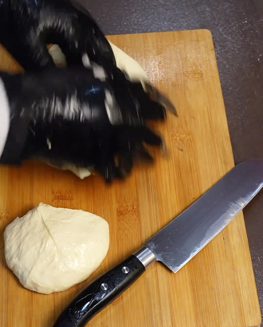 Four equal portions of pizza dough resting on a wooden cutting board next to a knife.