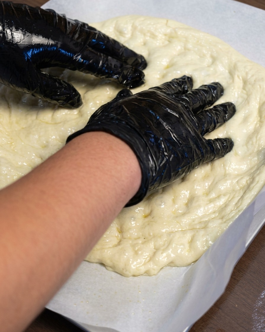 Hands stretching pizza dough outward on a sheet of parchment paper.