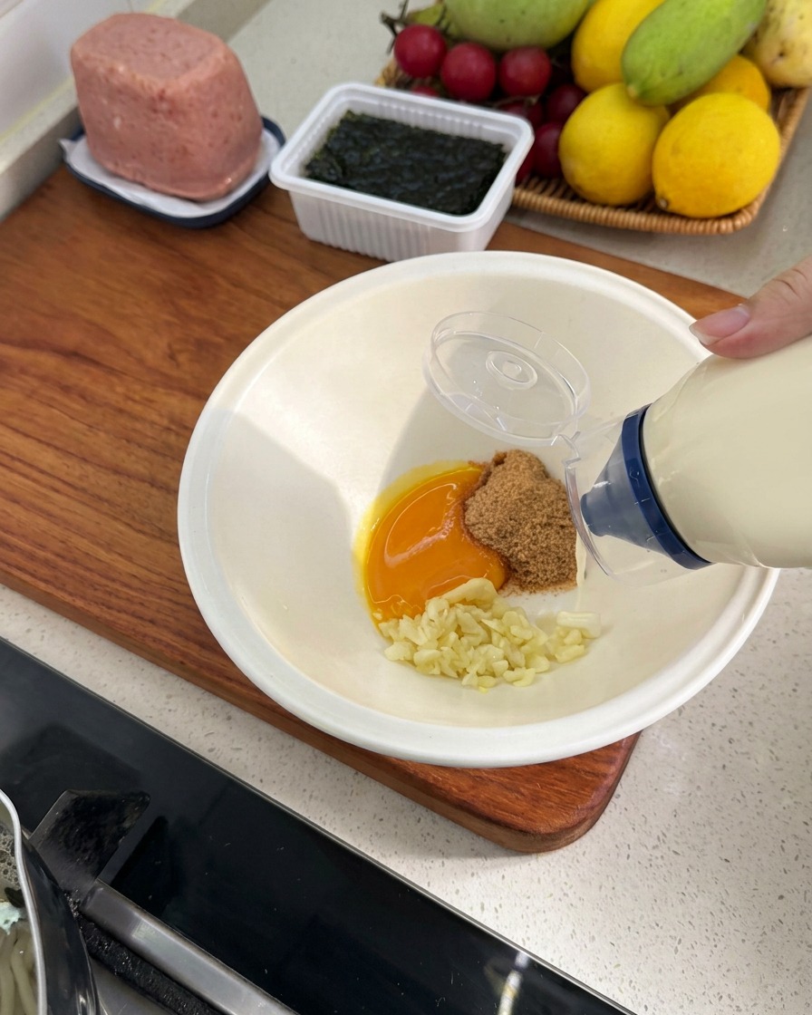 A squeeze bottle of mayonnaise adding a small amount of dressing into the bowl with the other ingredients.