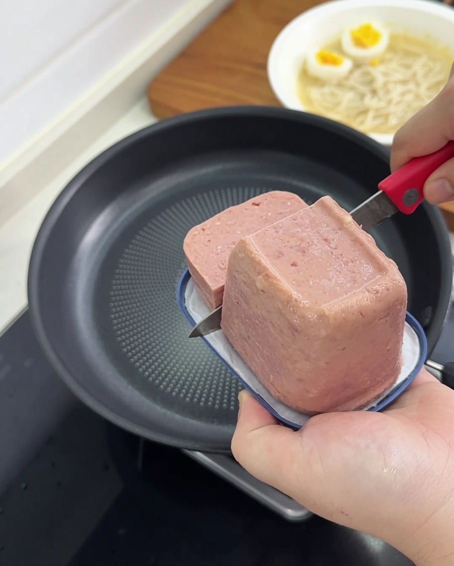Slices of luncheon meat frying in a non-stick pan until they reach a golden brown color.