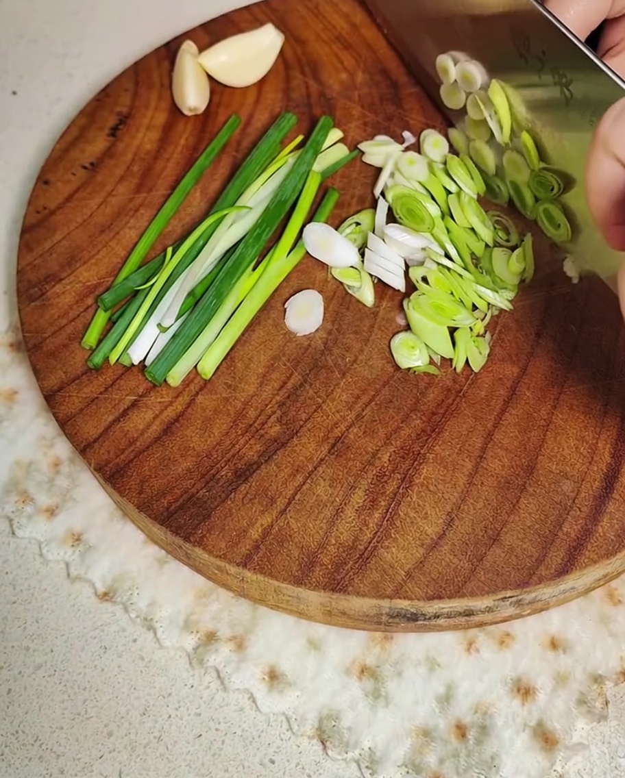 Green onions and garlic cloves being sliced on a wooden board.
