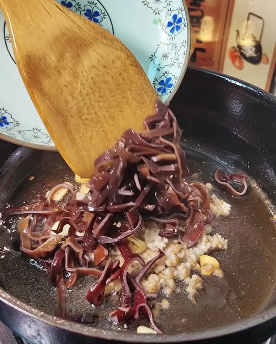 Minced meat and wood ear mushrooms being tossed in a frying pan with a wooden spatula.