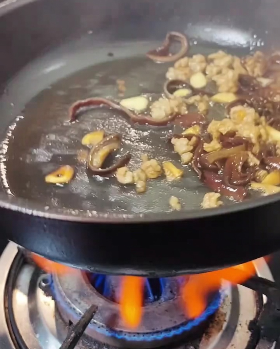 Light soy sauce and oyster sauce being drizzled into a pan containing meat and mushrooms.