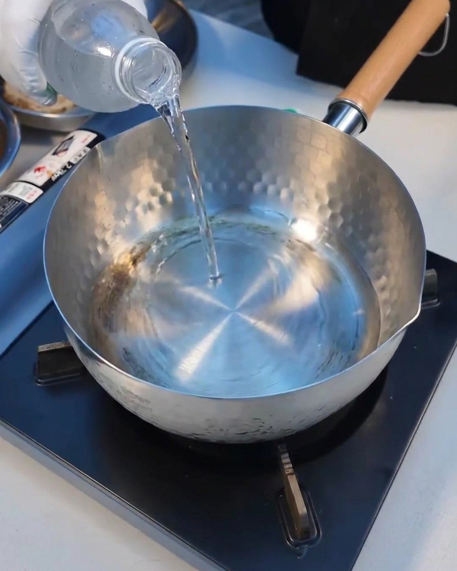 Mineral water being poured into a clean metal pot on the stove.