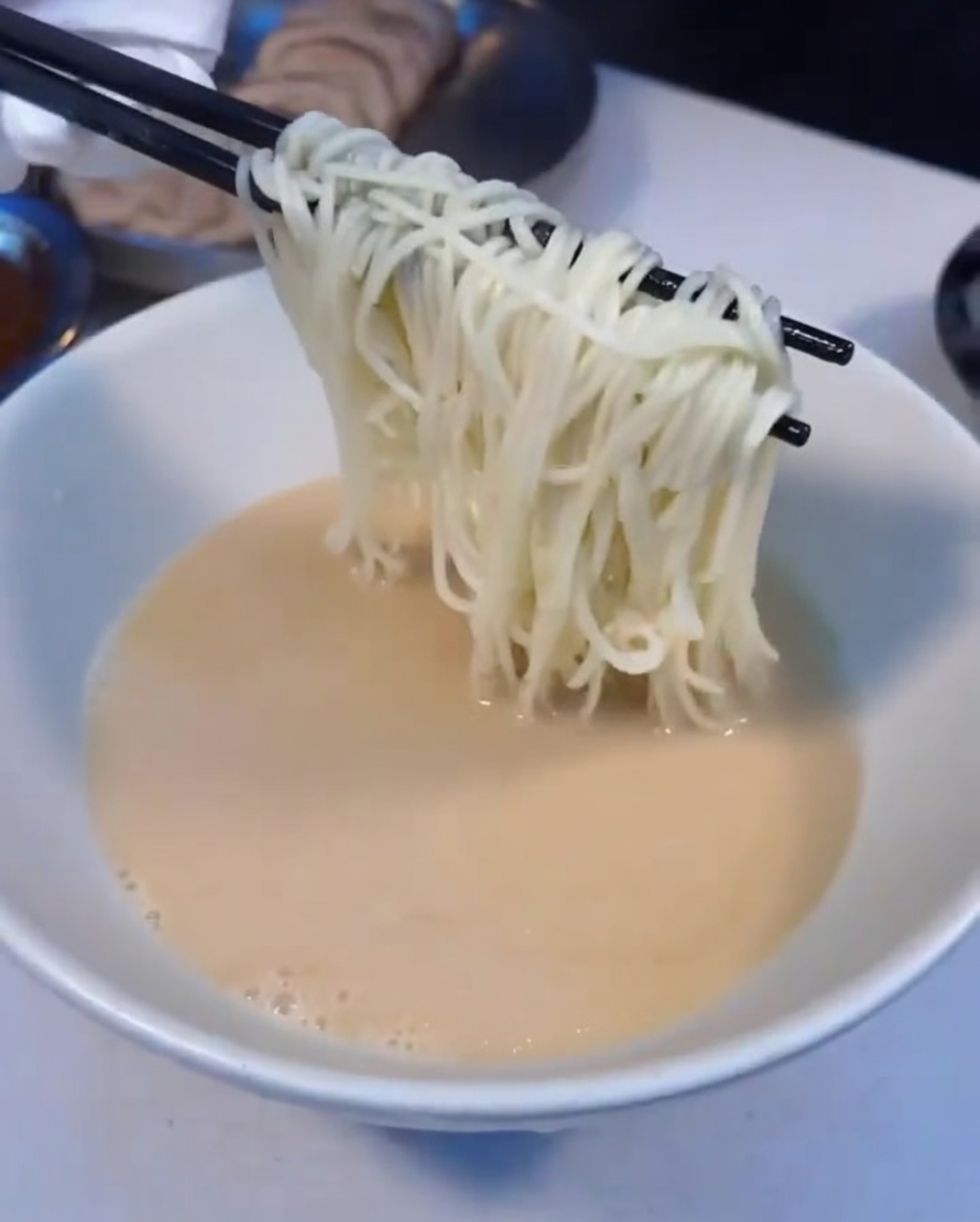 Steaming hot ramen noodles being transferred into a bowl of soup.