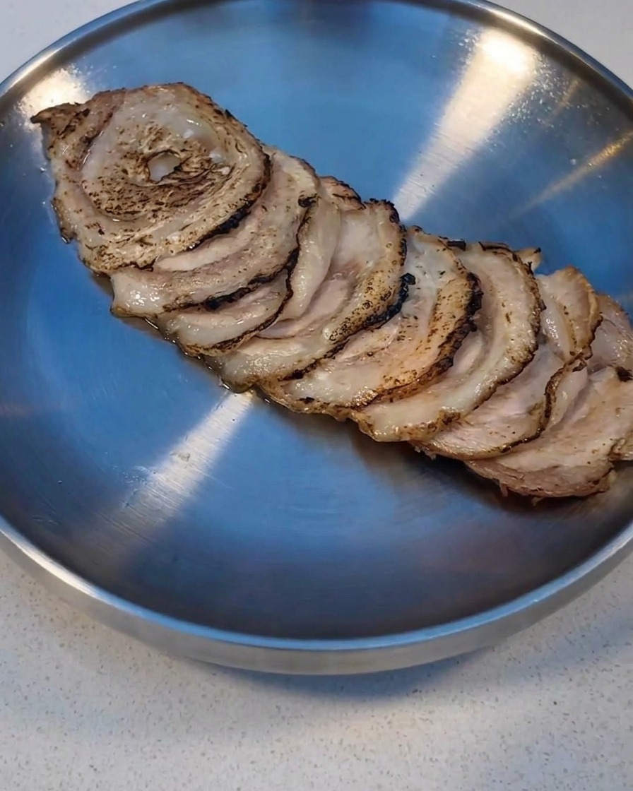 Char Siu slices being seared with a kitchen torch on a metal tray.