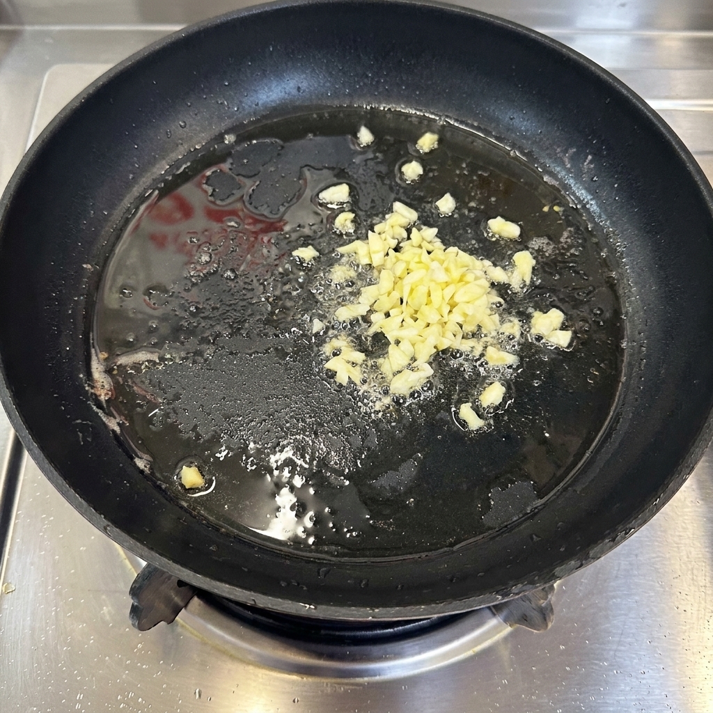 Finely minced garlic bubbling lightly as it fries in a thin layer of hot oil inside a black pan.