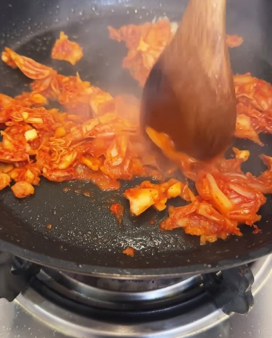 Water being poured into the pan containing sautéed kimchi and garlic.
