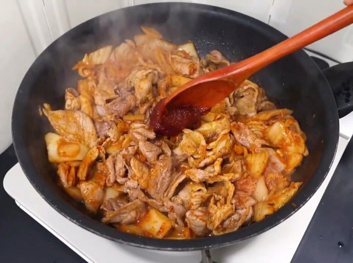 Chili paste and chili powder being mixed into the pork and kimchi stir-fry.