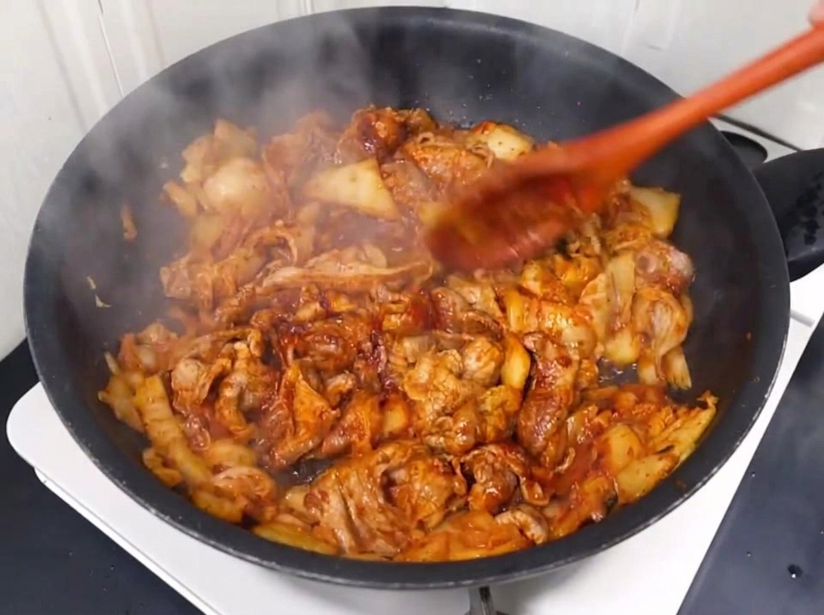 Water being poured into the pan with the stir-fried pork and kimchi.