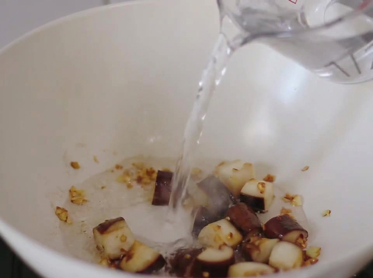 Water being poured into the pan containing sautéed mushrooms and garlic.