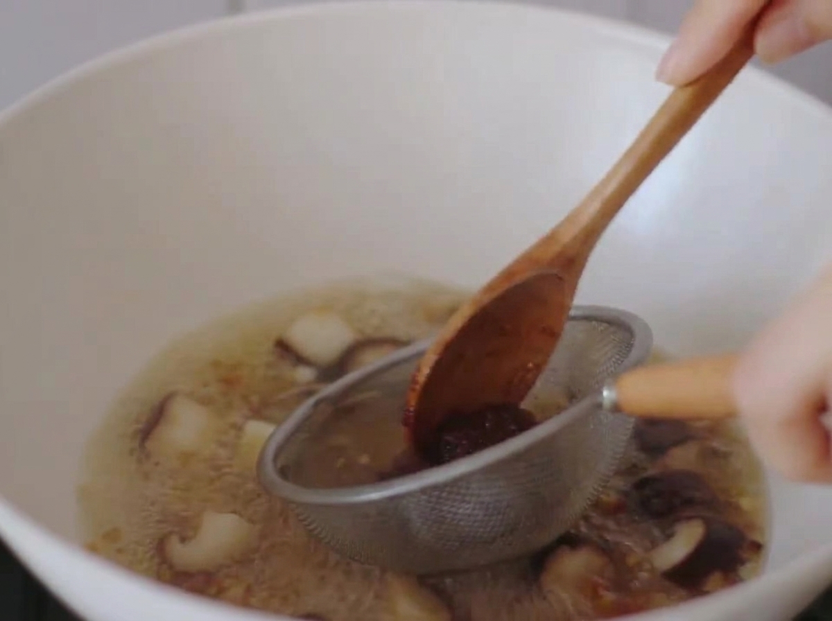 Miso paste being dissolved into boiling broth using a small metal strainer and a wooden spoon.
