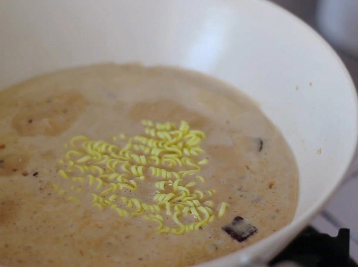 Instant noodles and narutomaki fish cake slices boiling in a creamy broth.