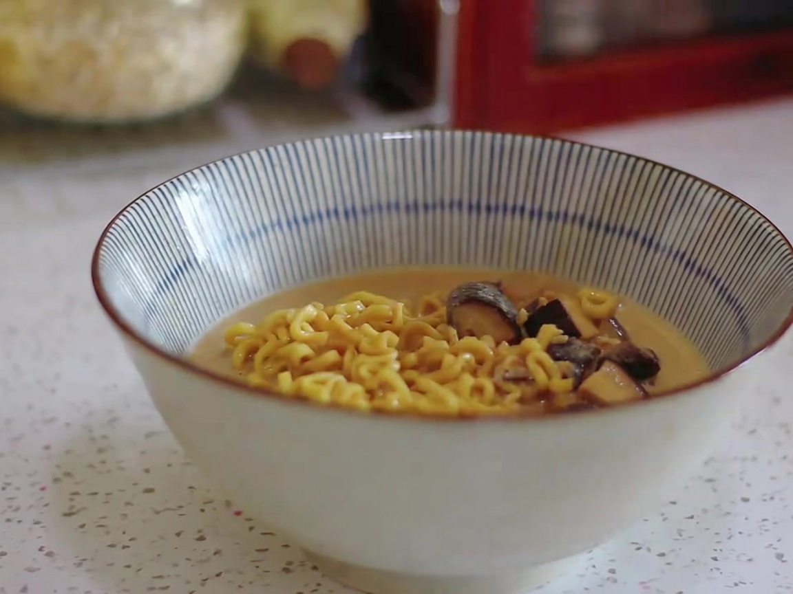 Ramen noodles and creamy broth being ladled into a striped serving bowl.