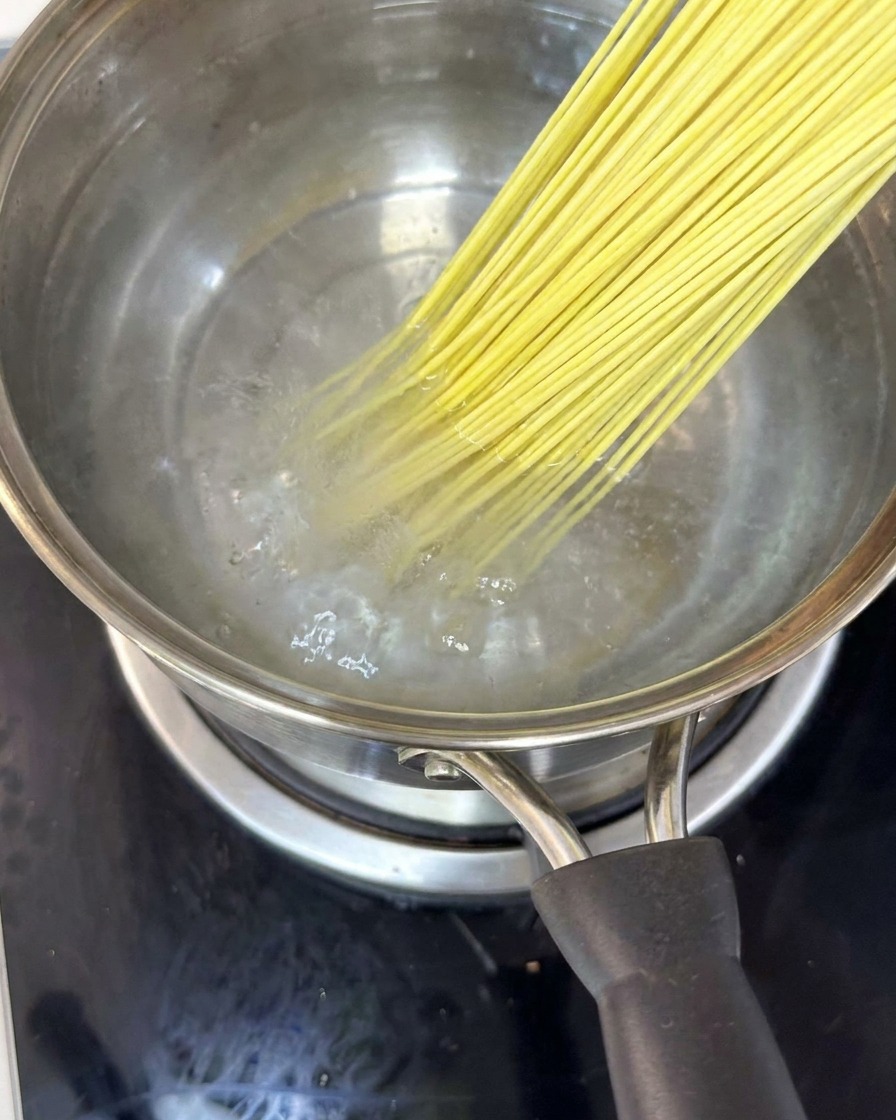 Noodles submerged in a pot of boiling water, being stirred with chopsticks.