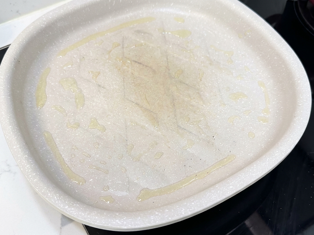 Bacon slices laid flat in a hot non-stick pan, beginning to cook.