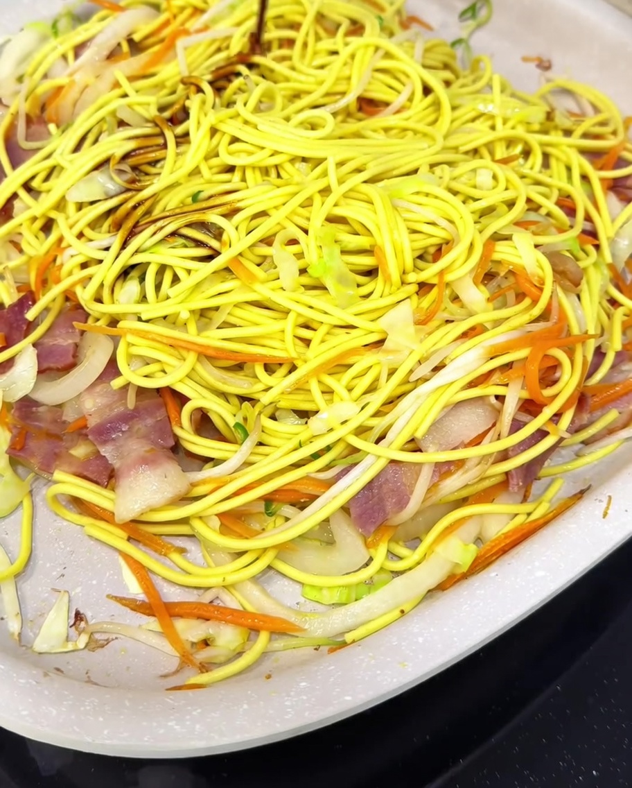 Noodles and vegetables being tossed in a pan with a blend of Worcestershire, oyster sauce, sake, and sugar.