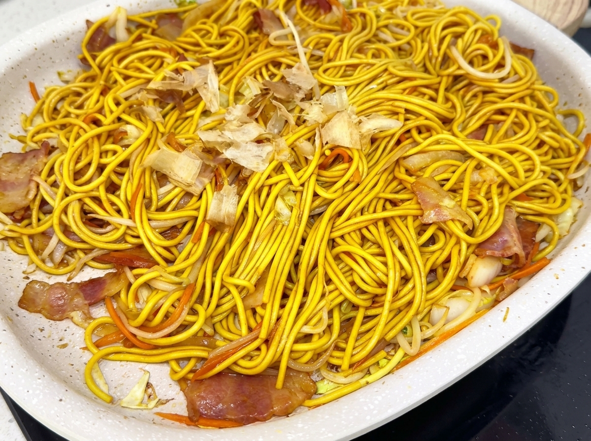 A pan full of stir-fried noodles topped with a scattering of bonito flakes.