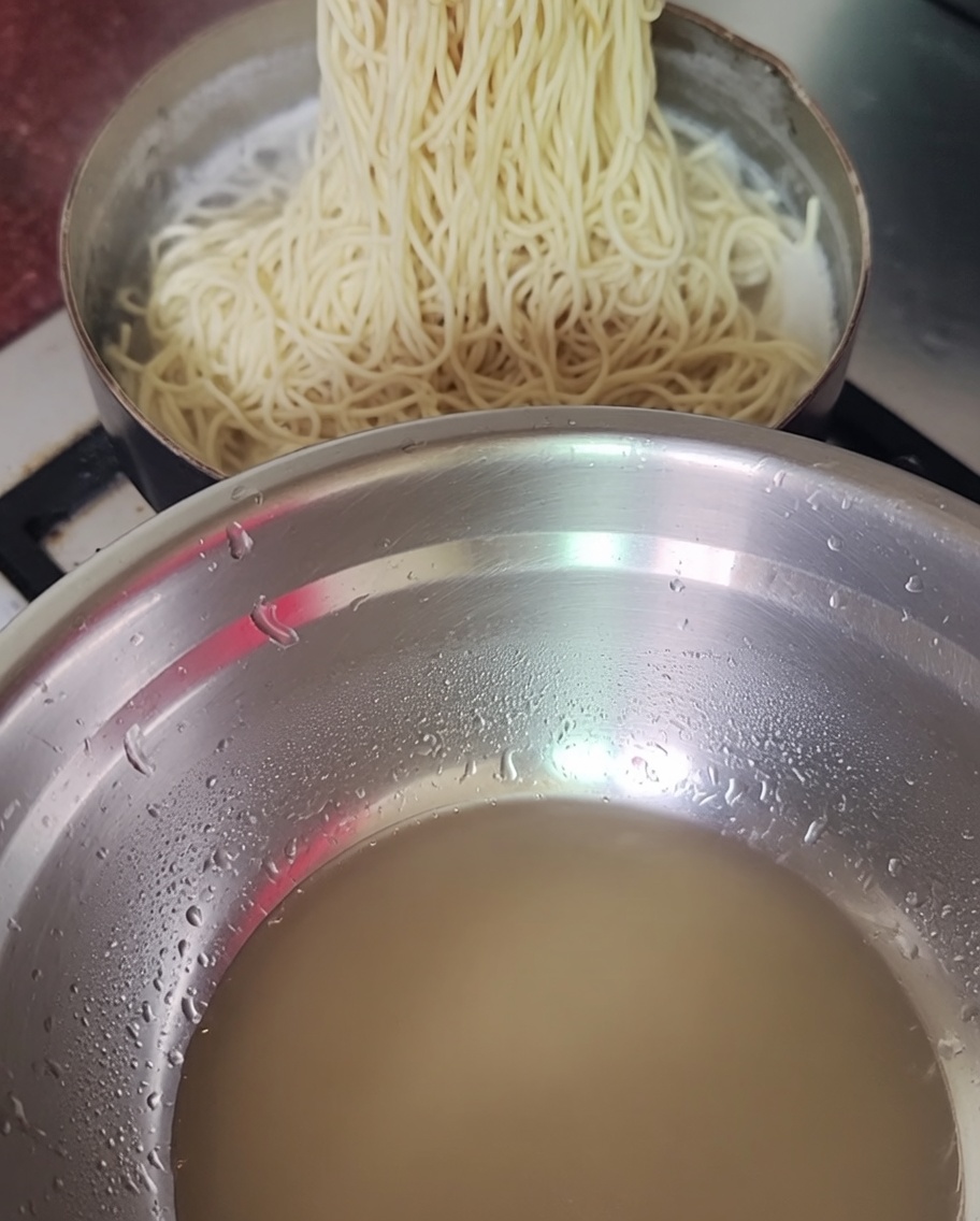 Cooked noodles being lifted from a pot with chopsticks.