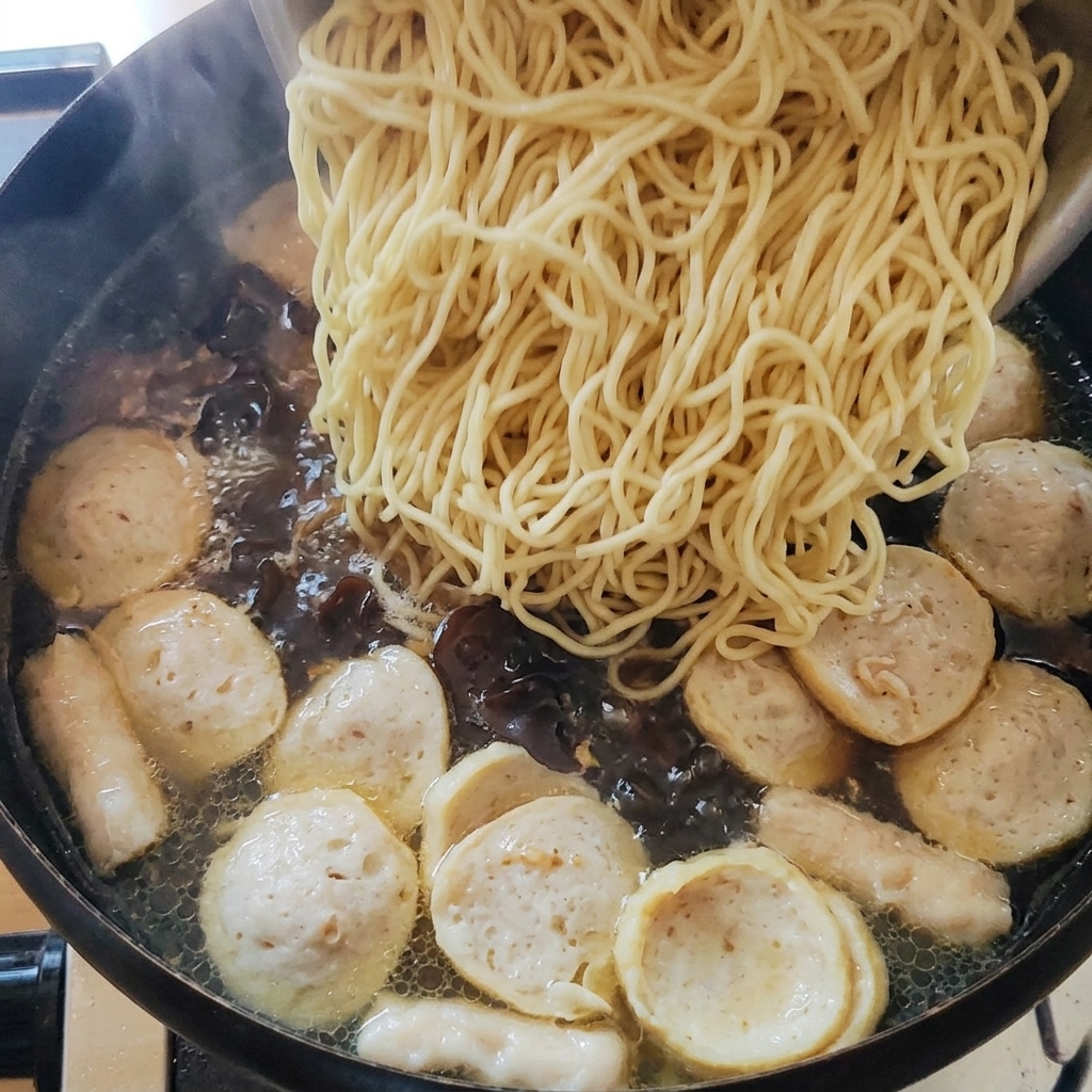 Cooked noodles being added to the pot of soup.