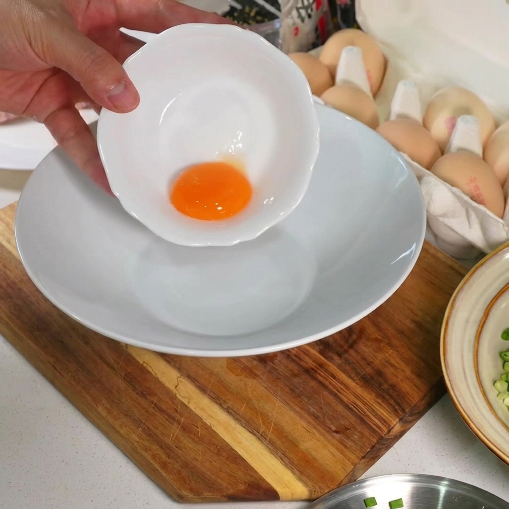 A single, vibrant raw egg yolk sitting at the bottom of a pristine white ceramic bowl.