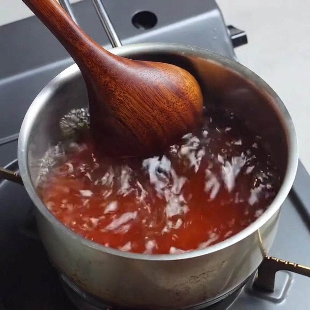 Seasoned ramen broth bubbling in a saucepan while being stirred.